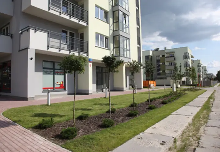 Nowoczesne budynki mieszkalne w stylu neowo bemowo z zielonymi skwerami i chodnikiem.