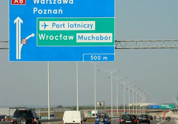 Znak drogowy pokazuje, jak dojechać na lotnisko we Wrocławiu z dworca PKP. Kierunek na lotnisko i Wrocław Muchobór jest po prawej stronie.