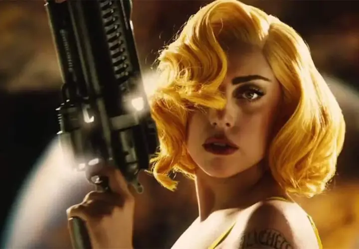 Lady Gaga med blont hår och en futuristisk pistol i en scen från en av hennes filmer.