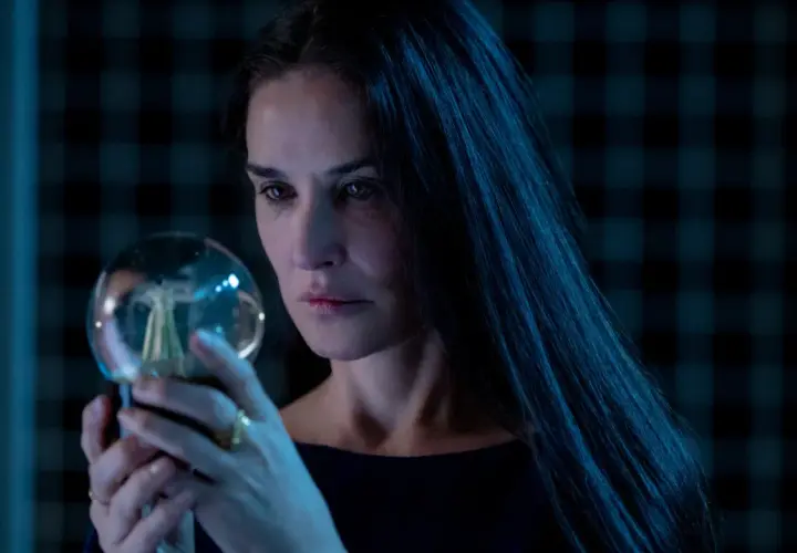 Donna con lunghi capelli scuri osserva una sfera luminosa, un'immagine che evoca mistero e riflessione, come in una recensione di "The Substance".