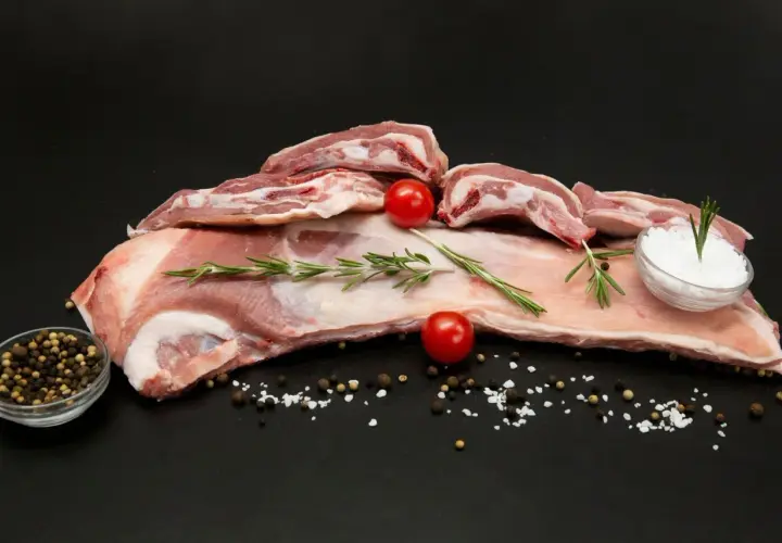 Poitrine d'agneau crue, parsemée de sel, poivre, romarin et tomates cerises, prête à être cuisinée.