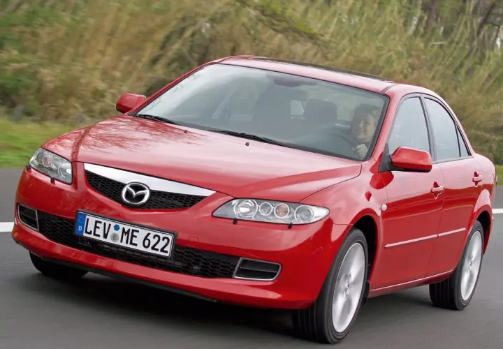 Czerwona Mazda 6 GG w ruchu, z uśmiechniętą kobietą za kierownicą, na tle zieleni.