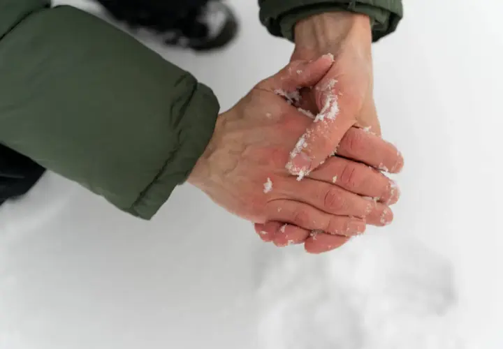 Händer med snö på, som gnuggas mot varandra för att värma upp torra handflator.