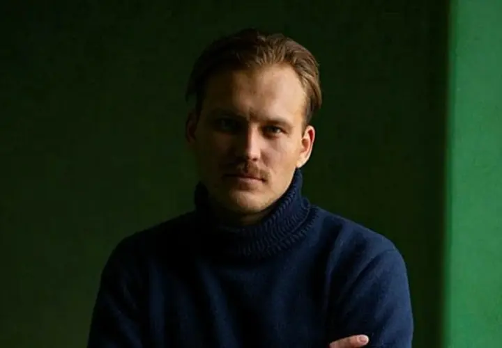 Pascal Engman, med mustasch och mörk polotröja, poserar framför en mörkgrön bakgrund.