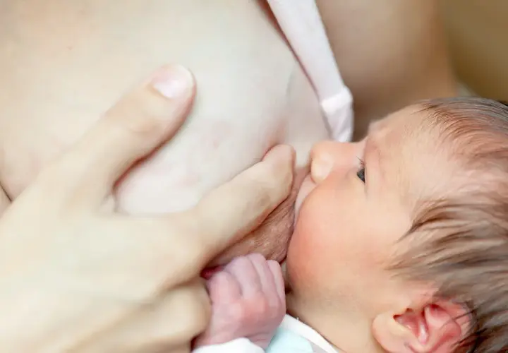 Un bébé tète le sein de sa mère. Une main soutient le sein, peut-être pour soulager les symptômes de mastite.