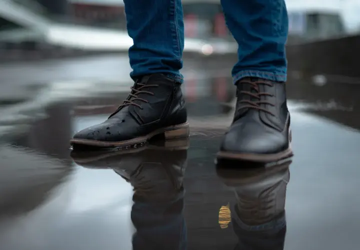 Man in jeans and black boots standing in a puddle. Learn how to rough up the bottom of slippery shoes for better grip.