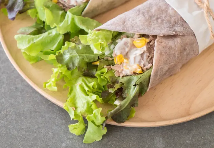 Pyszna tortilla z tuńczykiem, świeżą sałatą i kukurydzą, zawinięta w papier i przewiązana sznurkiem.
