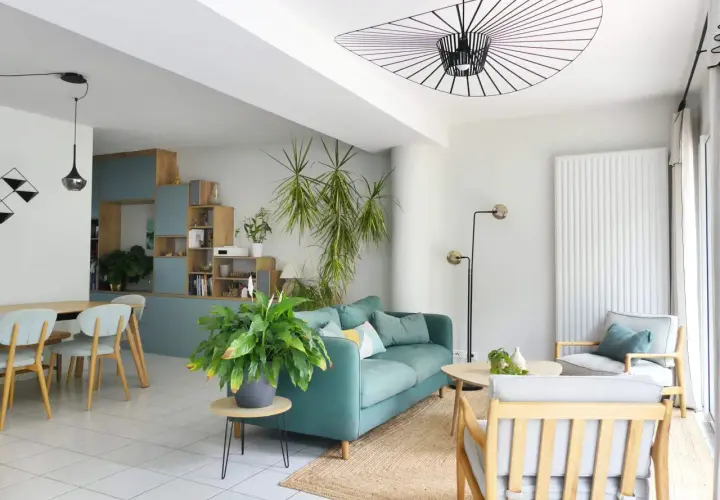 Aménagement de salon moderne avec canapé bleu sarcelle, fauteuil gris, table basse en bois et plantes vertes.