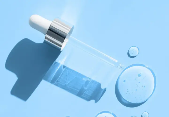 Droppe av serum med hyaluronsyra och retinol på blå bakgrund.