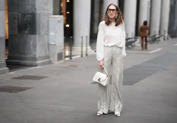 Elegancka kobieta w białej bluzce i srebrnych spodniach. Czy na komunie można ubrać się na biało? Ta stylizacja pokazuje, że tak, jeśli jest gustowna.