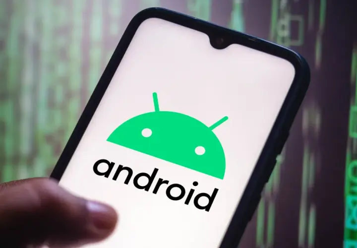 Dłoń trzyma smartfon z logo Android 10. W tle widać zielony, cyfrowy kod.