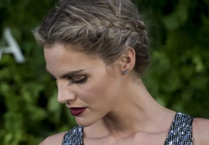 Mujer con elegante peinado con trenzas, maquillaje dramático y vestido brillante.