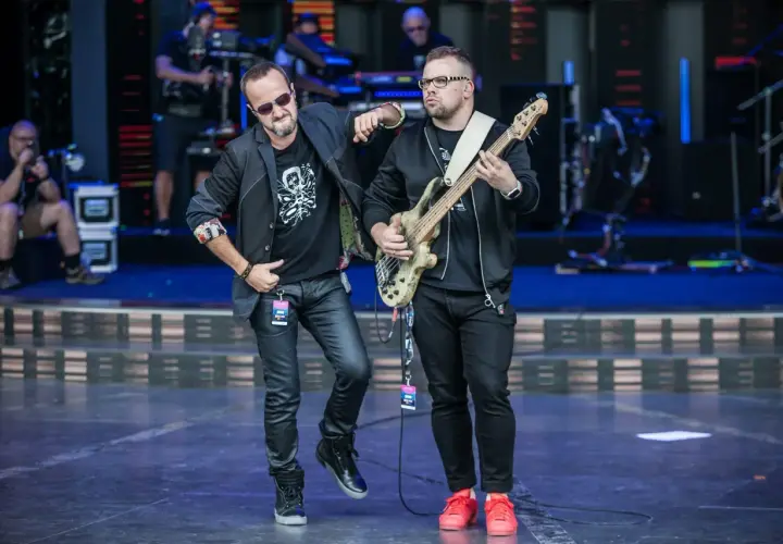 Dwóch muzyków na scenie, jeden z gitarą basową, drugi w okularach przeciwsłonecznych. Wyglądają jak nowy wokalista Kombi i jego kolega z zespołu.