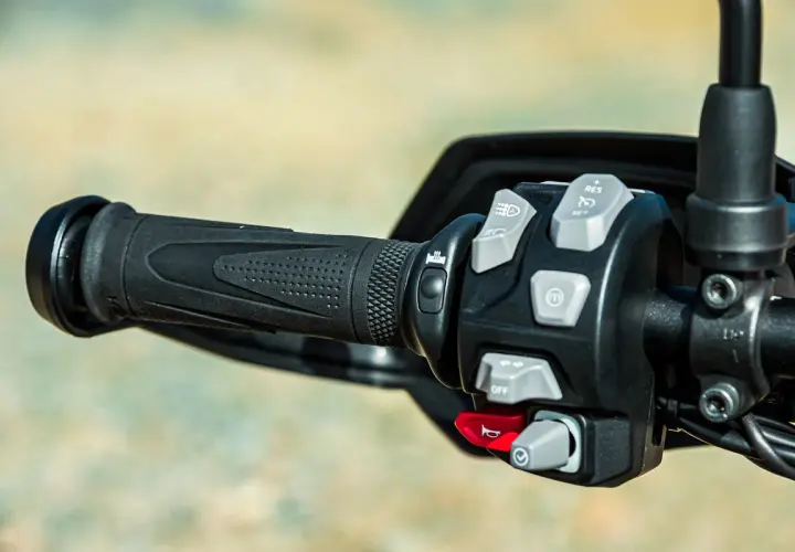 Mandos de la moto: puño negro texturizado y panel de control con botones grises y rojos para luces, crucero y bocina.