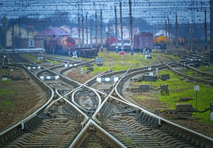 Skrzyżowanie torów kolejowych z widocznym wskaźnikiem W20. W tle stoją wagony towarowe.