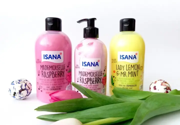 Trzy butelki ISANA: "Mademoiselle Raspberry" (różowa, z pompką i bez) i "Lady Lemon & Mr. Mint" (żółta). Obok kwiaty i ozdobne kule.