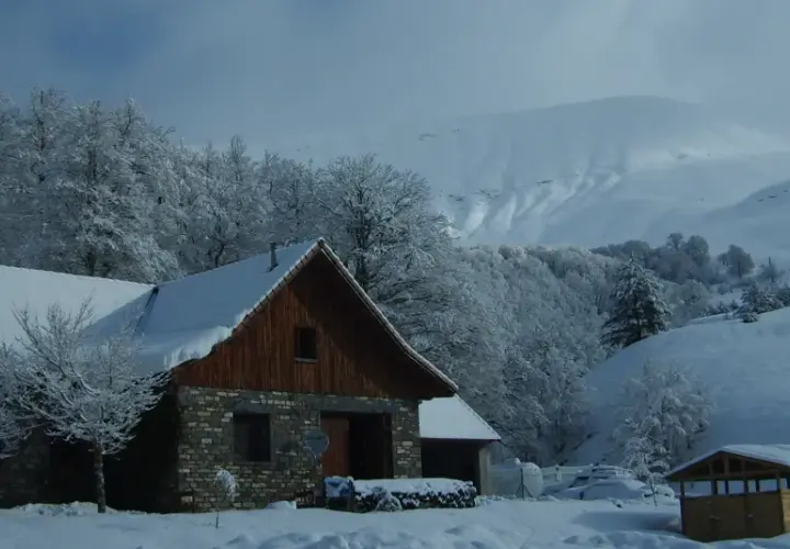 El refugio de Linza, cubierto de nieve, se alza entre árboles nevados y montañas imponentes.