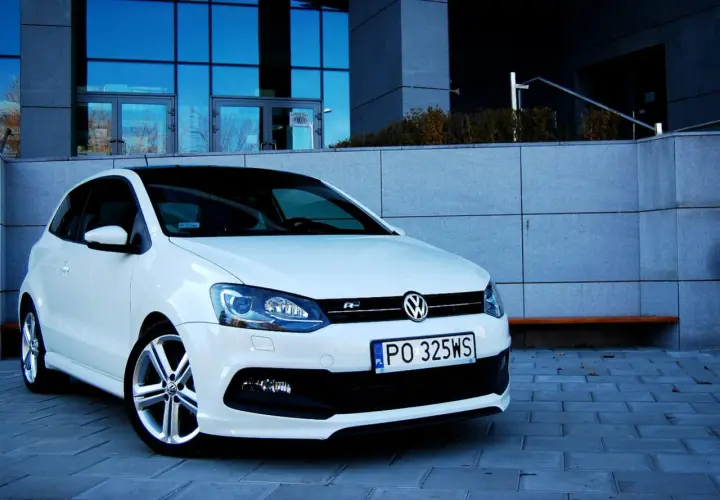 Biały VW Polo 1.2 benzyna z czarnym dachem, zaparkowany przed nowoczesnym budynkiem.