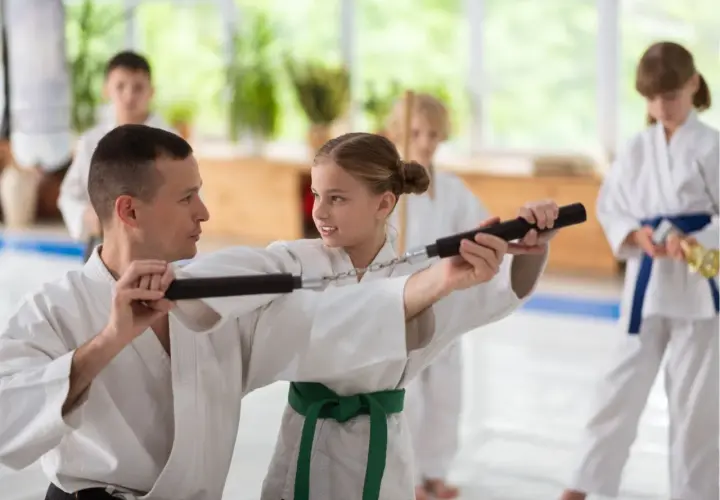 Nauczyciel pokazuje dziewczynce, jak używać nunchaku podczas treningu sztuk walki.