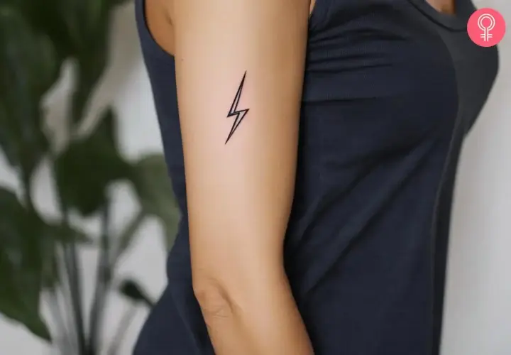 Minimalistyczny tatuaż piorun na ramieniu kobiety. Symbolizuje moc i energię.
