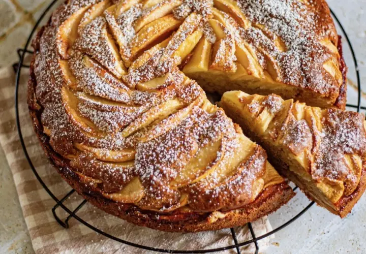 Un gâteau aux pommes et mascarpone irrésistible, saupoudré de sucre glace, avec une part coupée.