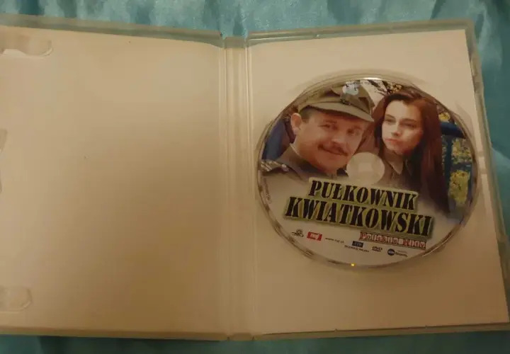 Płyta DVD z filmem "Pułkownik Kwiatkowski" i jego obsadą. Widoczni są główni bohaterowie, pułkownik i młoda kobieta.