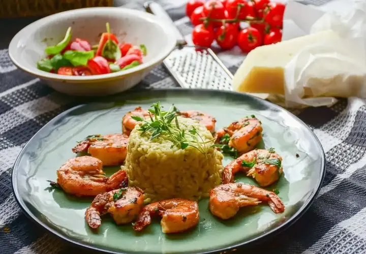 Krewetki z mlekiem kokosowym i curry na risotto, udekorowane ziołami. Obok miseczka z pomidorkami i bazylią, ser i tarka.