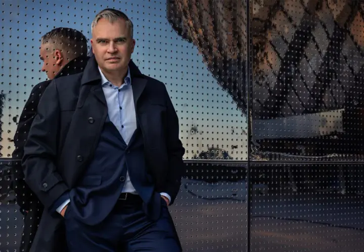 Jerker Virdborg står framför en reflekterande fasad, klädd i kostym och rock.