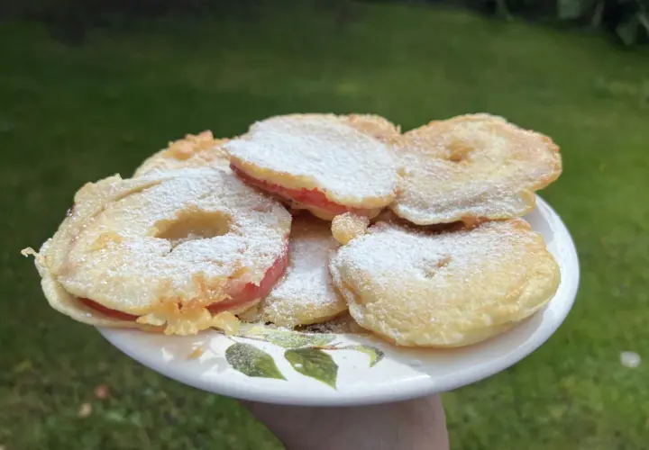 Słodkie jabłka w cieście, posypane cukrem pudrem, czekają na spróbowanie na talerzyku z liśćmi.