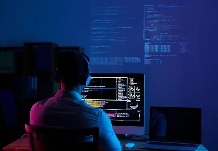 Młody człowiek w słuchawkach pochłonięty kodowaniem na ekranie. To idealne miejsce do nauki cyberbezpieczeństwo studia.