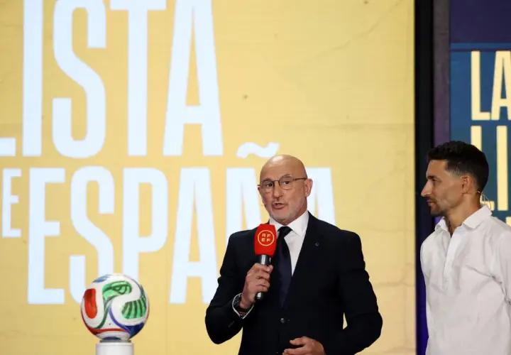 Mężczyzna w garniturze z mikrofonem i piłkarze Hiszpanii na tle napisu "LISTA DE ESPAÑA".