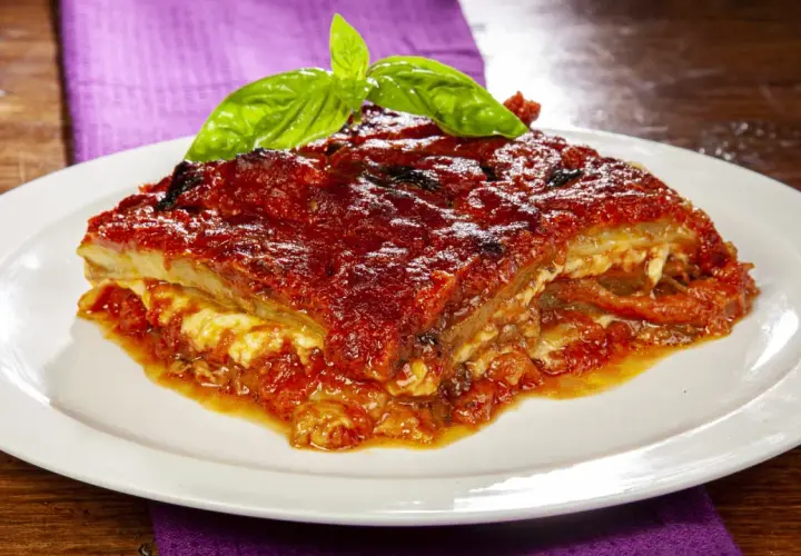 Una fetta di parmigiana di melanzane napoletana, ricca e saporita, guarnita con basilico fresco.