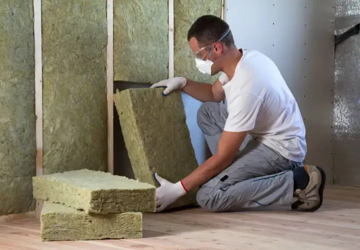 Operaio con maschera e occhiali installa pannelli isolanti per un cappotto interno.