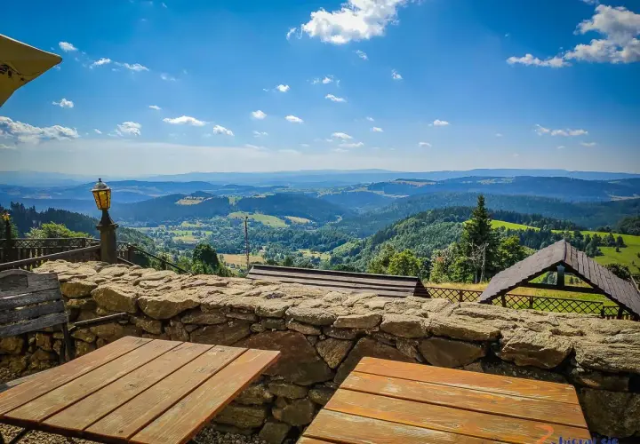 Widok z góry Sowa na malownicze wzgórza. Drewniane stoły i kamienny murek zapraszają do podziwiania panoramy.