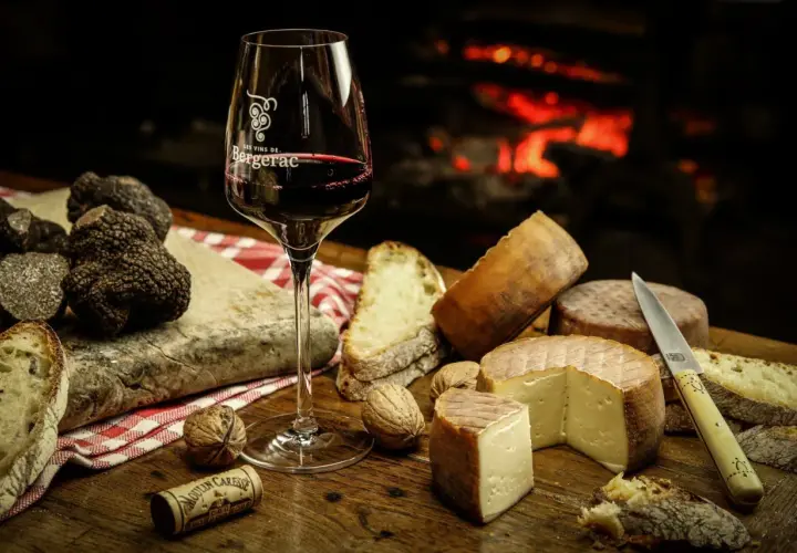 Verre de vin rouge, truffes noires, fromages et pain sur une table en bois, près d'une cheminée. Un délice pour accompagner un vin avec truffade.