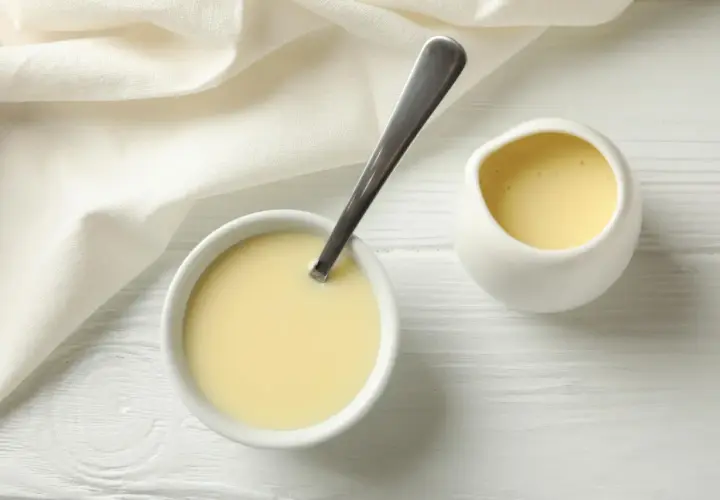 Crema amarilla en un cuenco con cuchara y jarrita, ideal para sustituir nata para cocinar por leche en recetas ligeras.