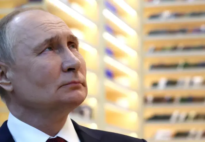 Nahaufnahme von Wladimir Putin, der nachdenklich in die Ferne blickt. Die Hintergrundbeleuchtung deutet auf eine Veranstaltung hin, vielleicht im Zusammenhang mit den Russland Wahlen.