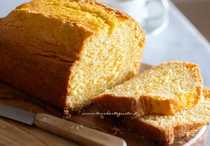 Plumcake senza yogurt dorato e soffice, tagliato a fette su un tagliere di legno con un coltello.