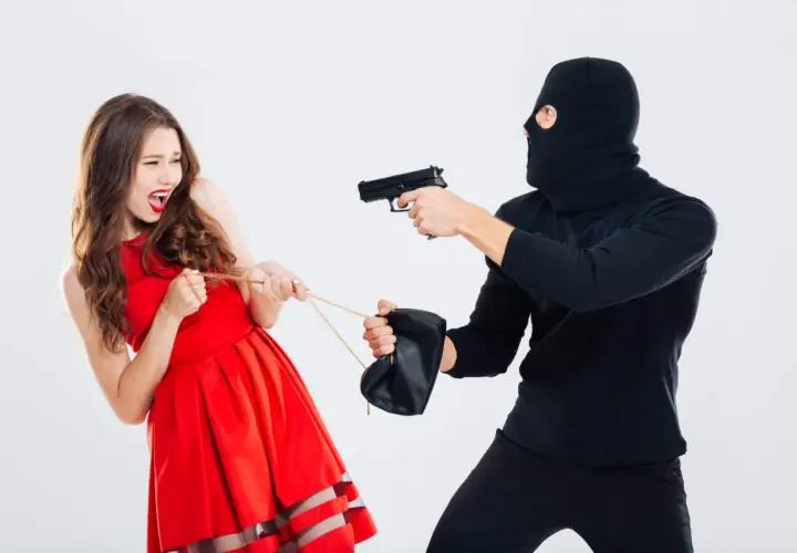 Una mujer con vestido rojo grita mientras un ladrón enmascarado le apunta con una pistola y tira de su bolso. Es como soñar que te roban.