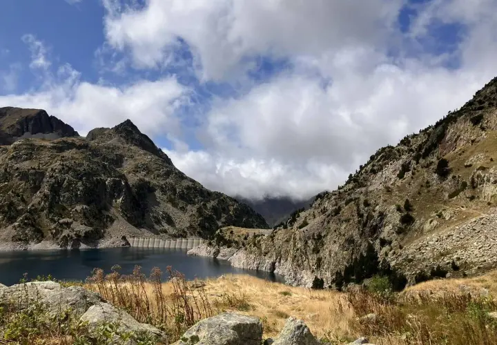 Paisaje montañoso con un embalse azul, ideal para rutas en Sallent de Gállego. Nubes y vegetación agreste completan la escena.