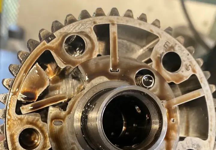 Widok z bliska na koła zmiennych faz rozrządu, z widocznymi elementami mechanicznymi i śladami oleju.