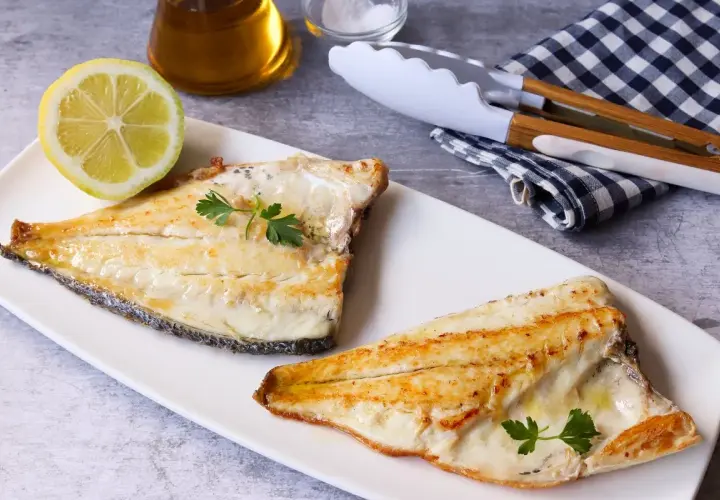 Dos filetes de dorada a la plancha, jugosos y dorados, servidos con perejil fresco y una rodaja de limón.