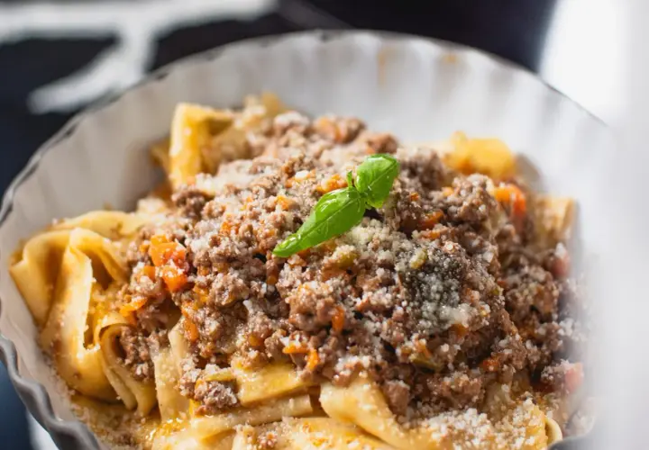 Un plat de pâtes fraîches, garni d'une sauce bolognaise riche et savoureuse, parsemé de parmesan et d'une feuille de basilic. Une recette spaghetti bolognaise italienne authentique.