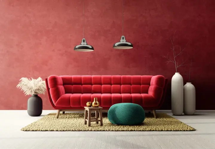 Soggiorno moderno con divano rosso vellutato e **effetto spugnato muro** color bordeaux. Due lampade a sospensione, pouf verde acqua e vasi bianchi completano l'arredo.