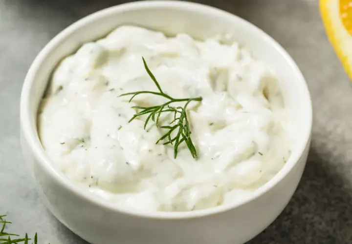 Salsa yogurt ricetta cremosa con aneto fresco e una fetta di limone sullo sfondo.