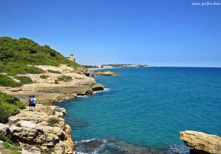Dos personas caminan por el camí de ronda en Tarragona, disfrutando de las vistas al mar Mediterráneo y la costa.