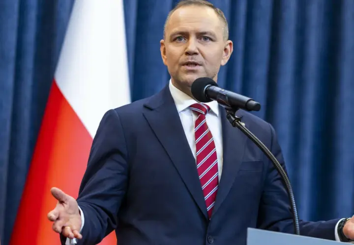 Mężczyzna w garniturze przemawia przy mikrofonie na tle flagi Polski. Czy prezydent faktycznie planuje ogłosić stan wyjątkowy w związku z sytuacją na wschodzie?