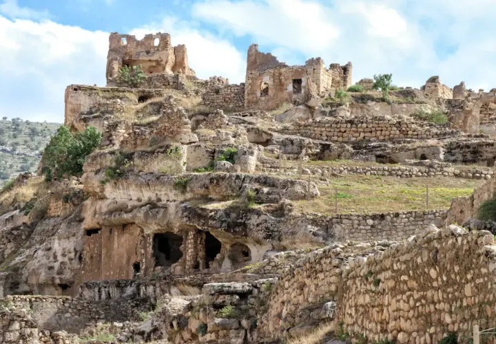 Ruiny starożytnego miasta Hasankeyf na skalistym zboczu, z widocznymi jaskiniami i kamiennymi murami.