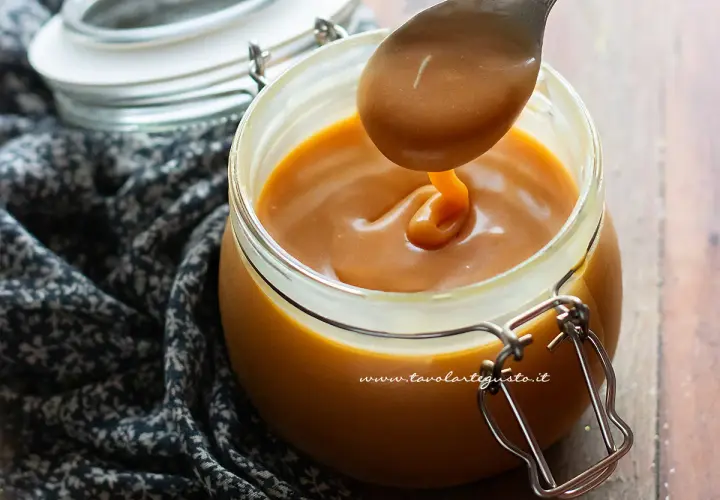 Caramello salato ricetta: un cucchiaio raccoglie la salsa dorata da un barattolo di vetro.