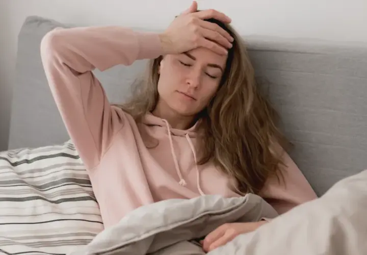 En kvinna med handen på pannan i sängen, känner ångest på morgonen.